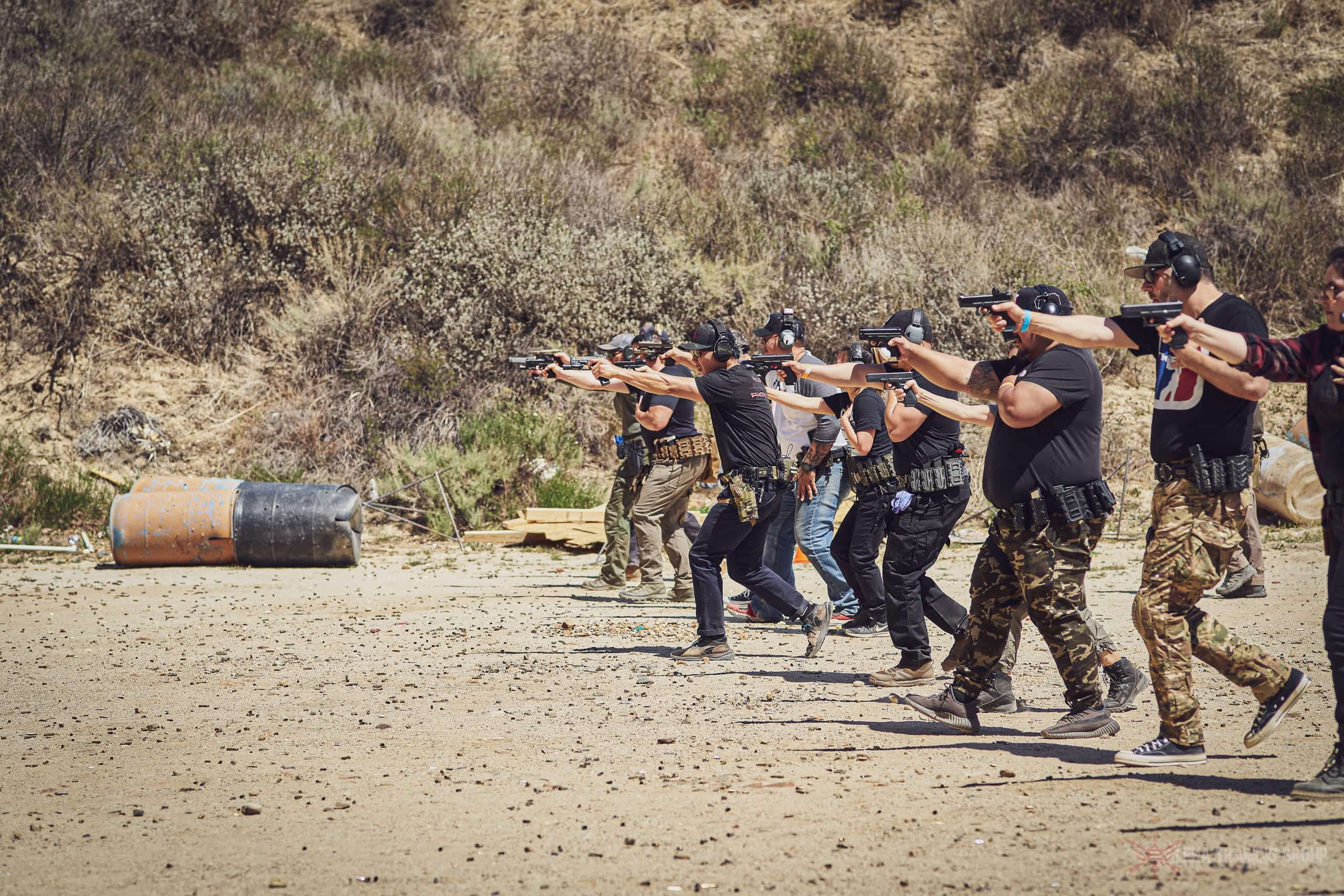 A line of students presenting pistols together on an outdoor range