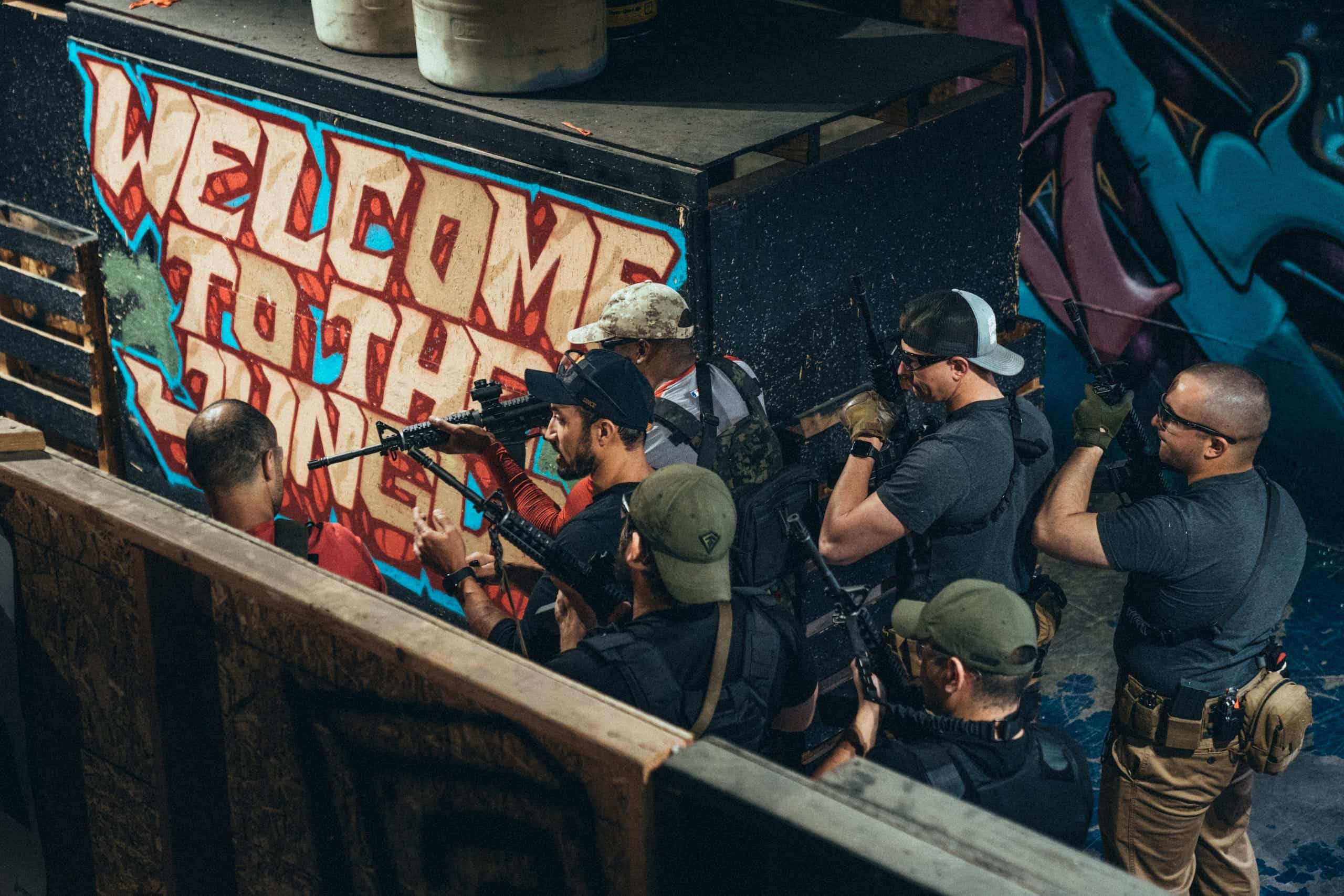 A team stacked along a graffiti-covered wall, carbines up, waiting to make entry