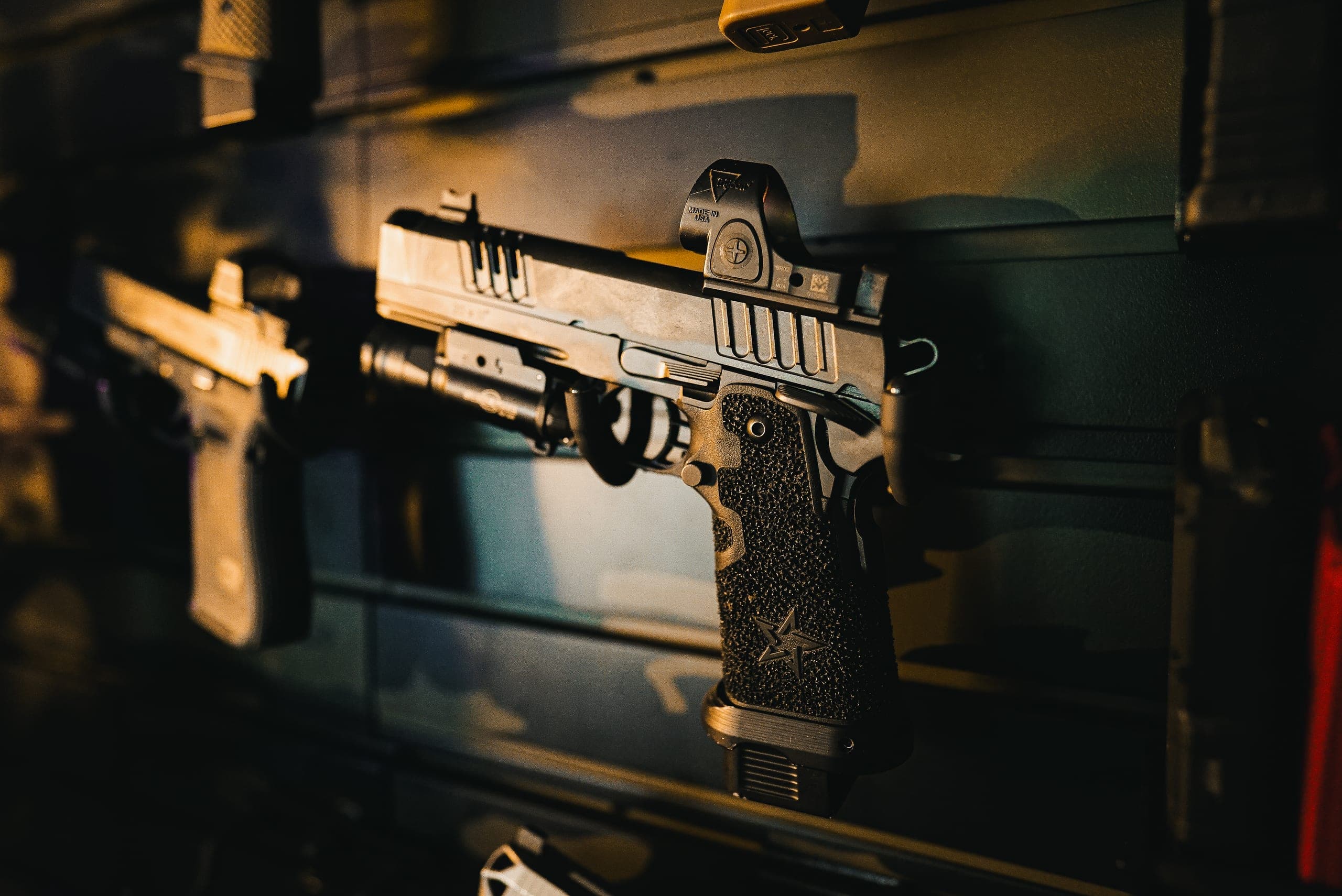 A pistol fitted with a mini red dot sight, lit warm against a dark wall