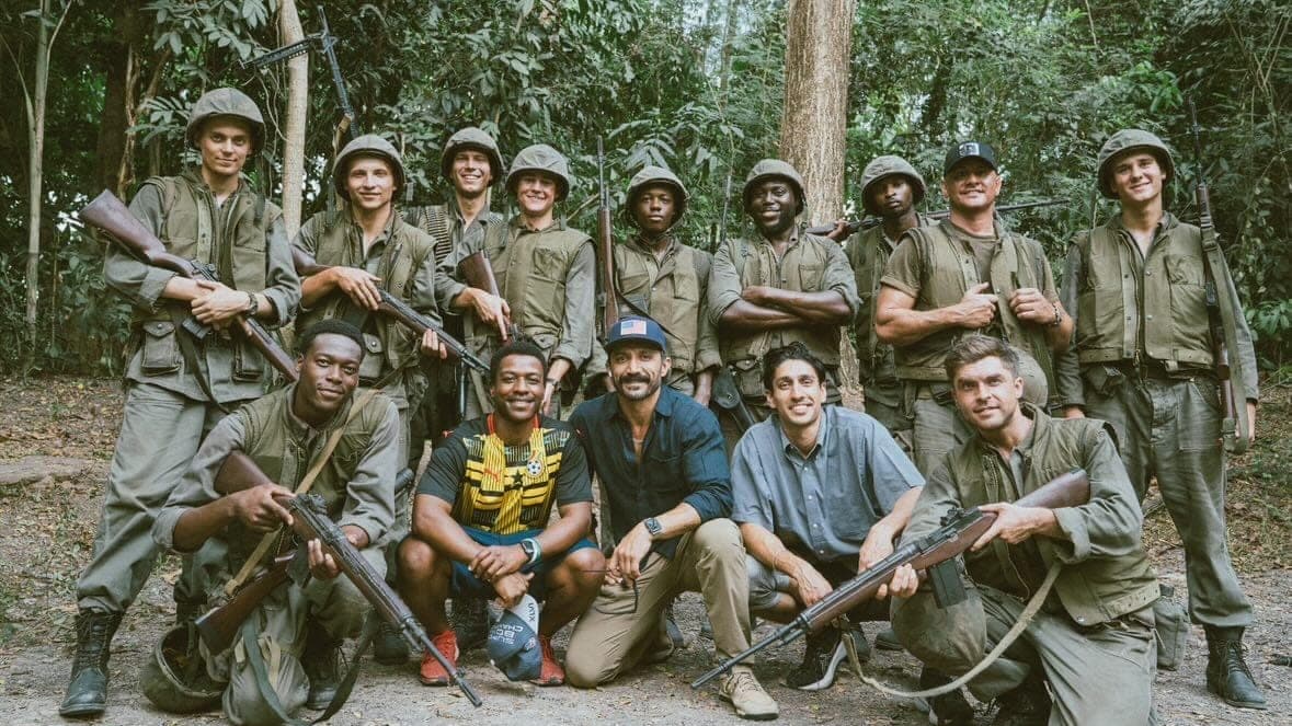 Cast in Vietnam-era uniform on a jungle set, with the advisory team crouched in front