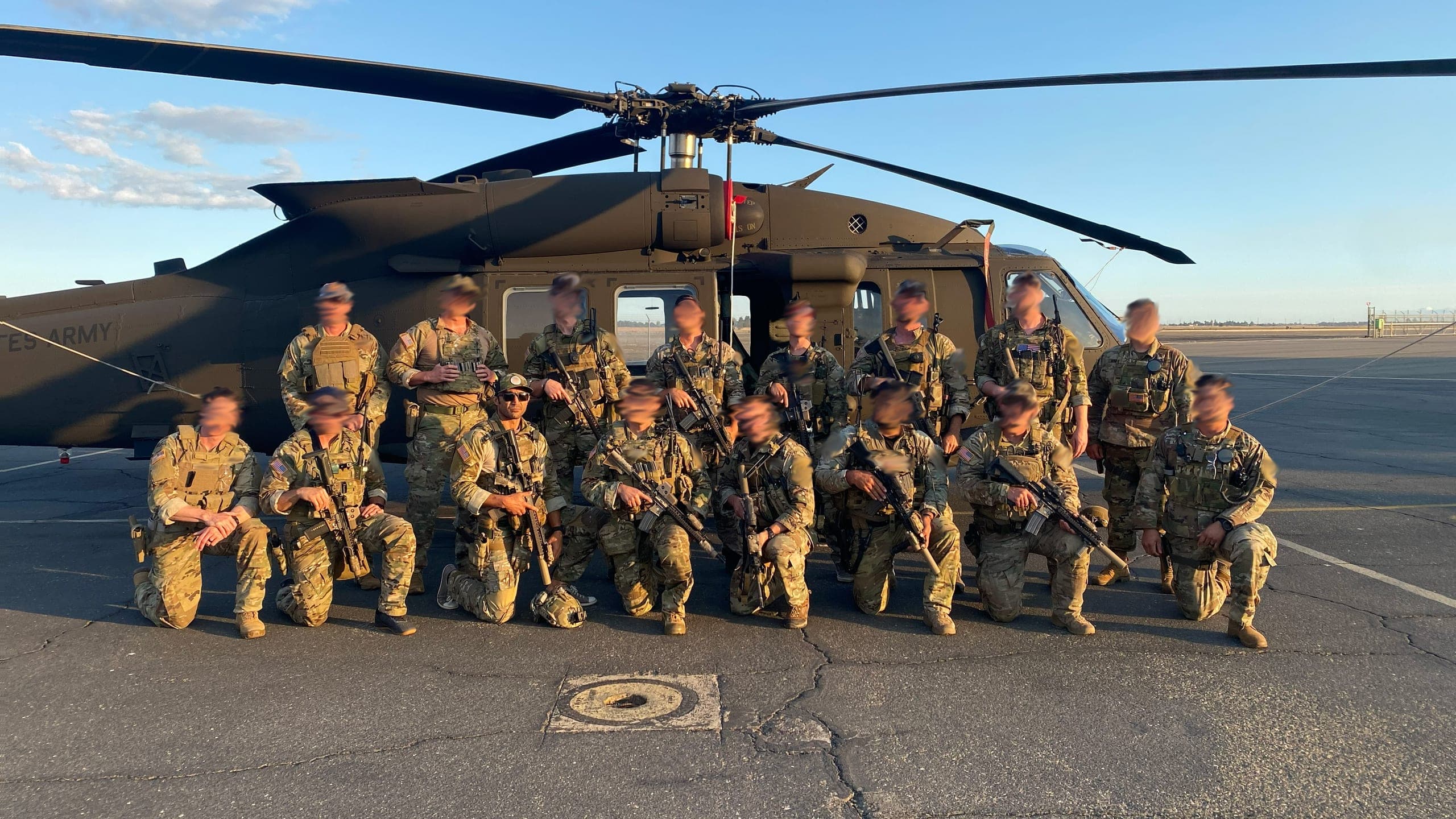 A 2ATG team in multicam, kneeling and standing in front of a UH-60 Black Hawk on the flight line