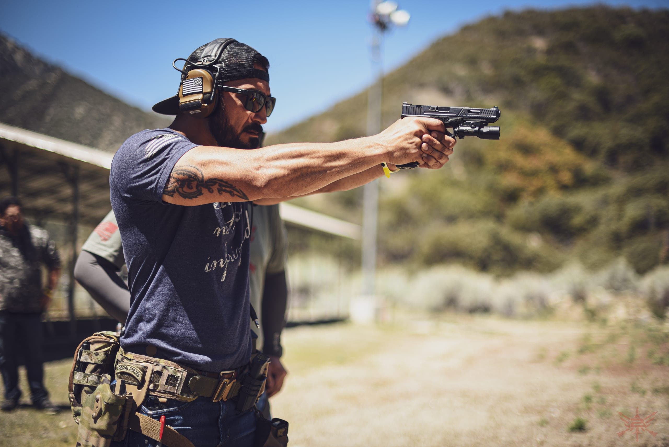 A shooter in ear protection presenting a pistol two-handed on an outdoor range