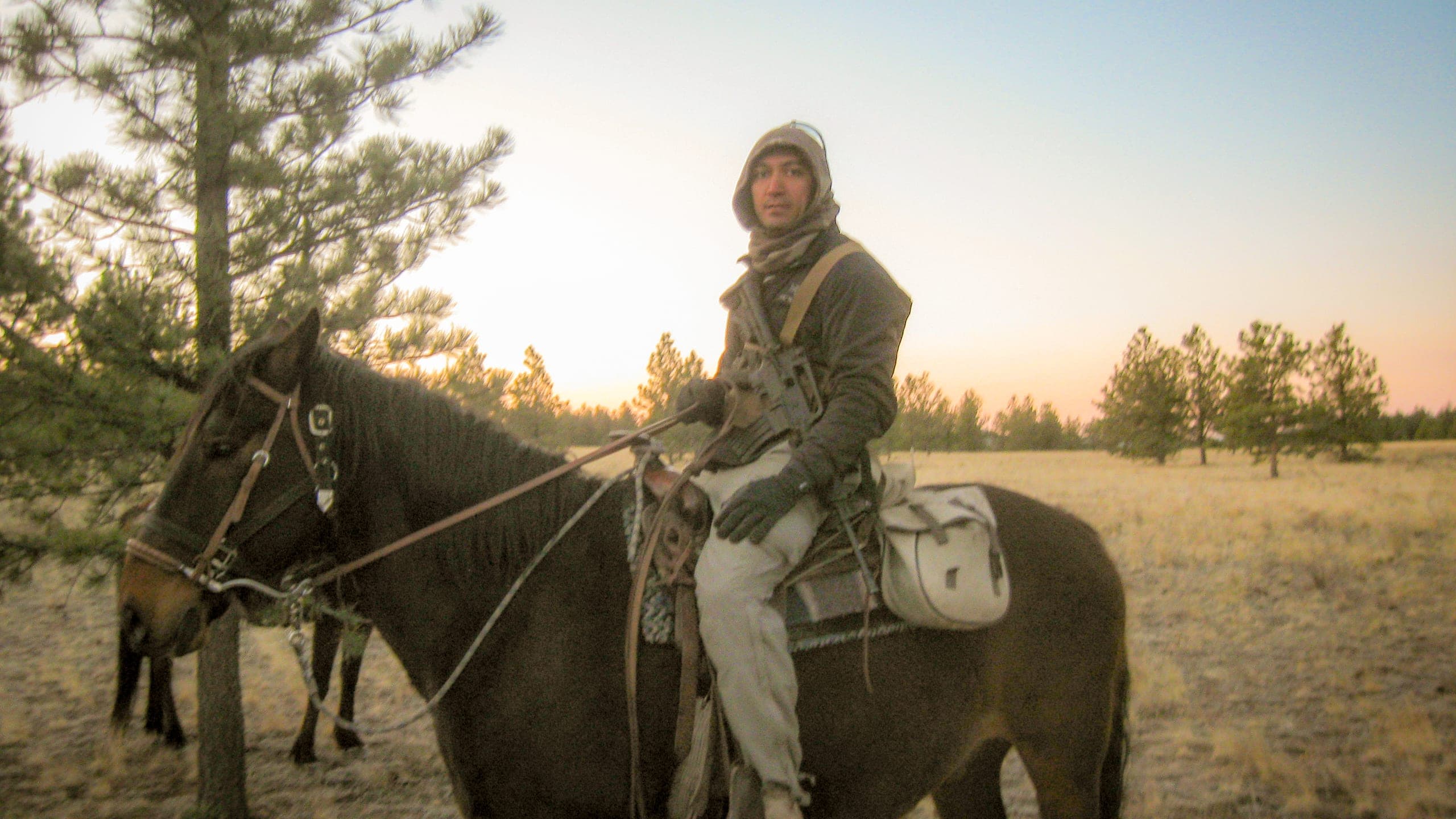 On horseback in cold-weather gear, crossing open grassland at first light