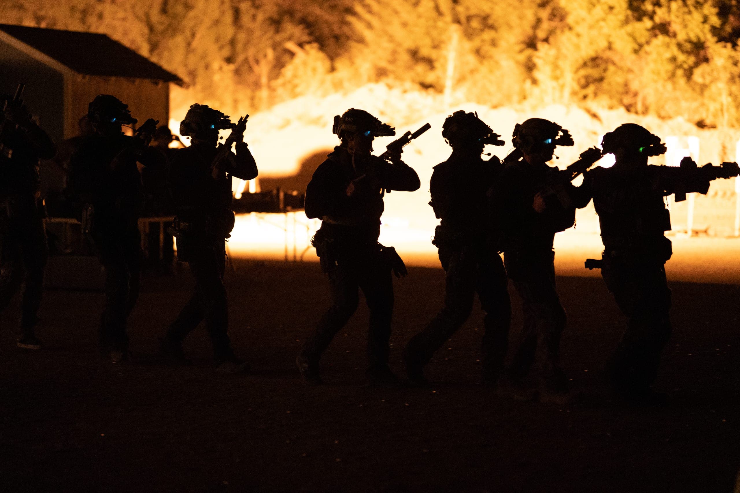 A team moving in silhouette under night vision, lit from behind by burning ground